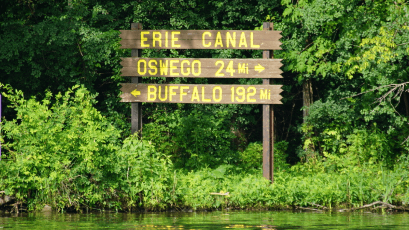 Erie Canal wooden sign by lush shoreline on canal boat route