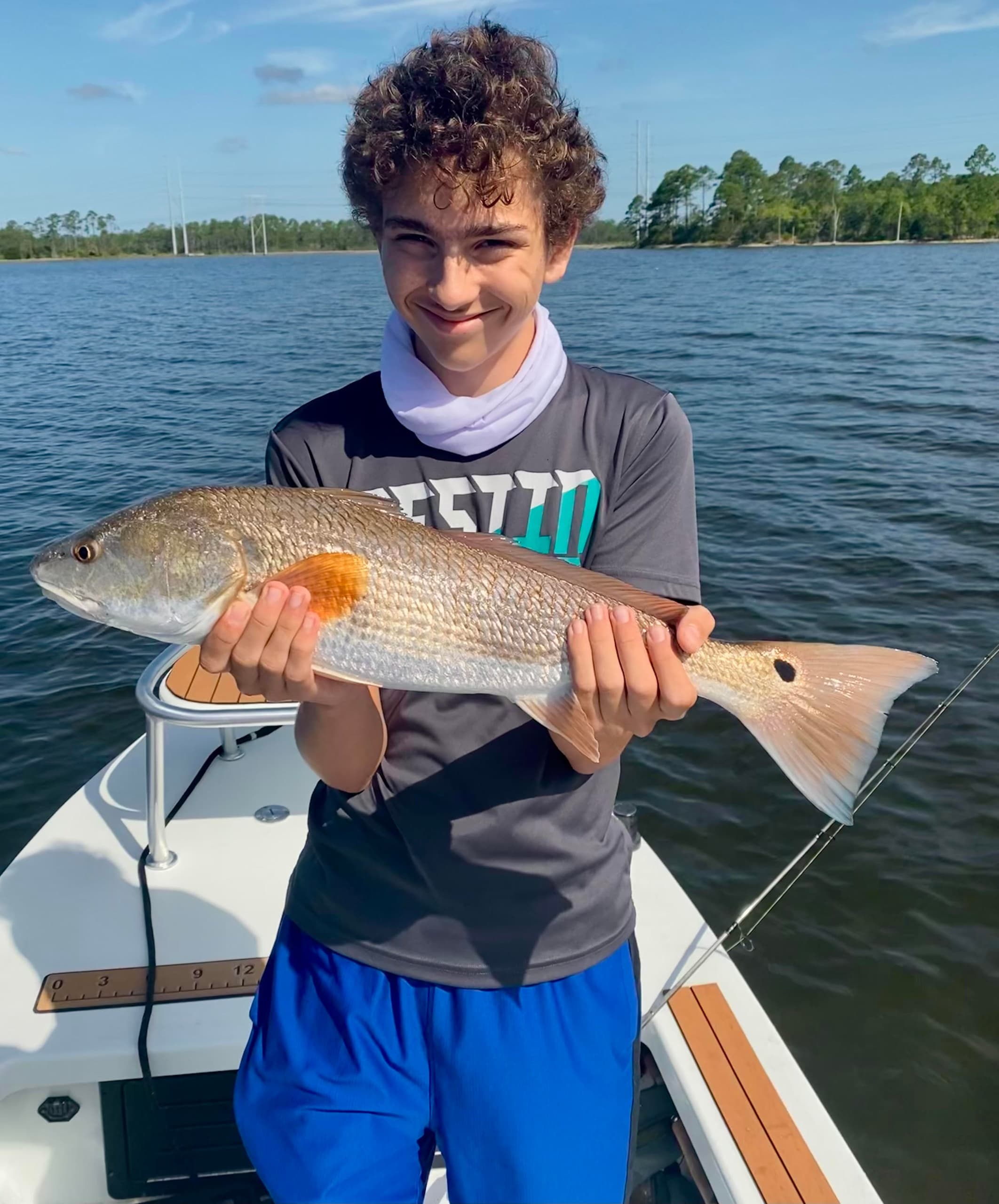 Teen angler holding redfish aboard flats fishing boat