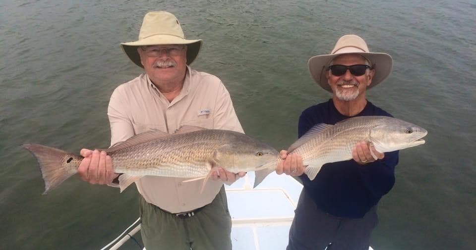 Two anglers holding redfish on deck, inshore coastal fishing and smiles