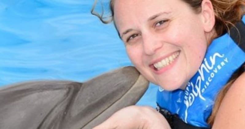 Smiling guest touching dolphin during guided marine encounter