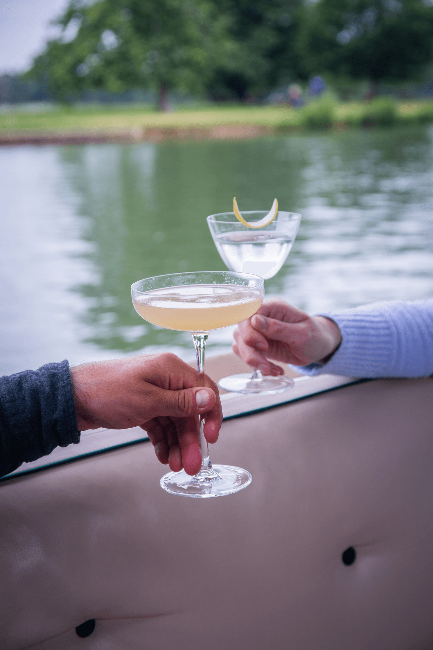 Two cocktails held by riverbank aboard Oxford cruise boat