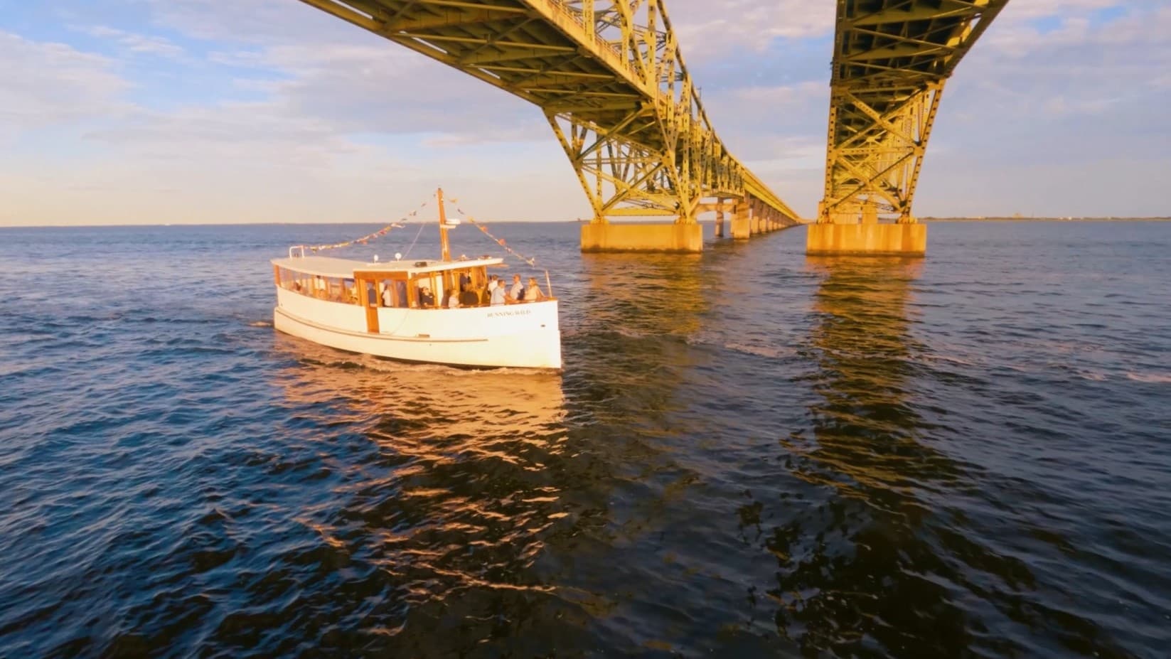 Sightseeing boat cruising under coastal bridge at sunset