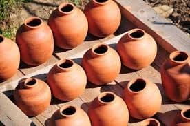 Rows of terracotta pots drying in sunny outdoor pottery yard