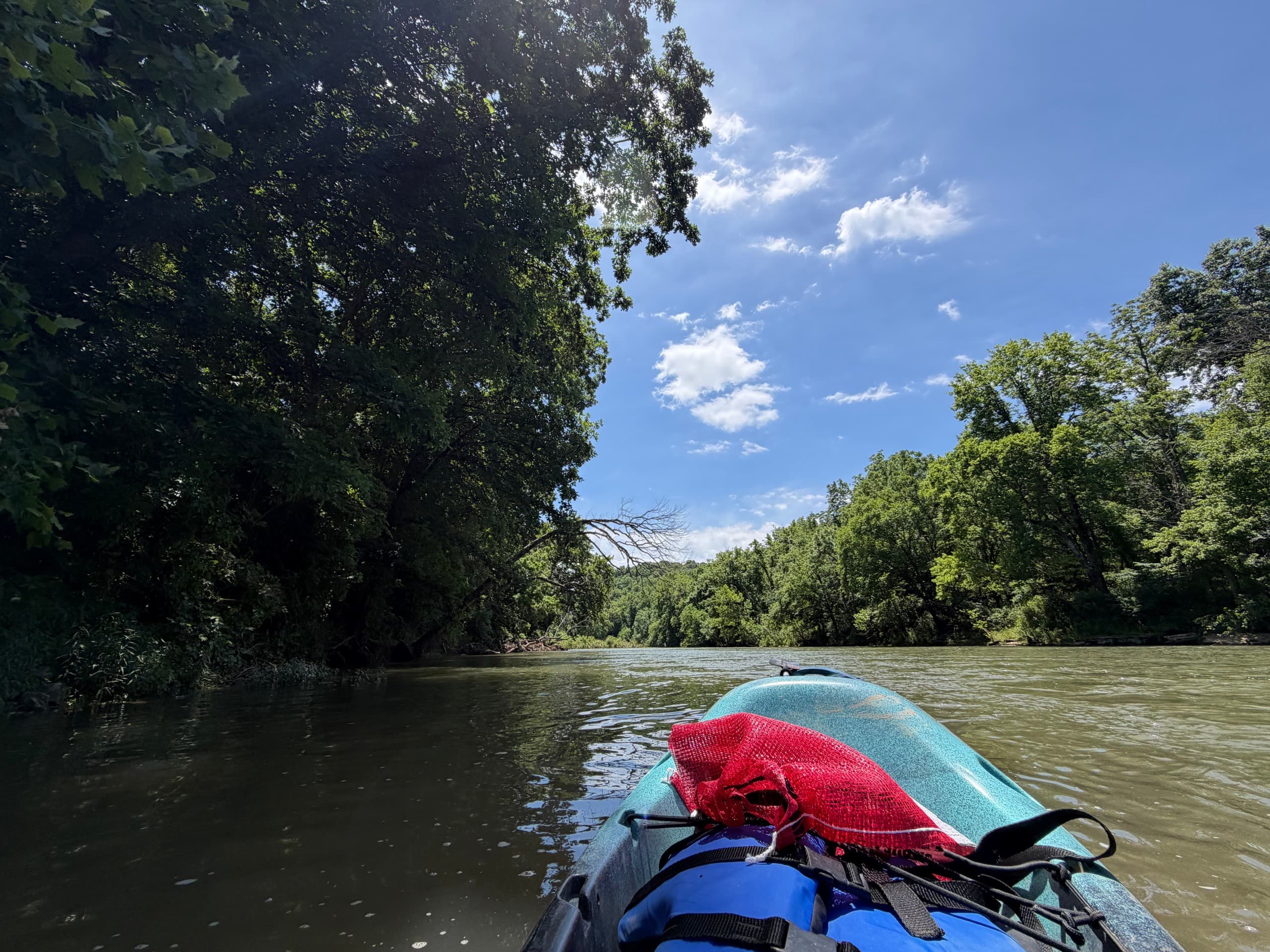 Kayak bow view paddling a calm tree-lined river on sunny day