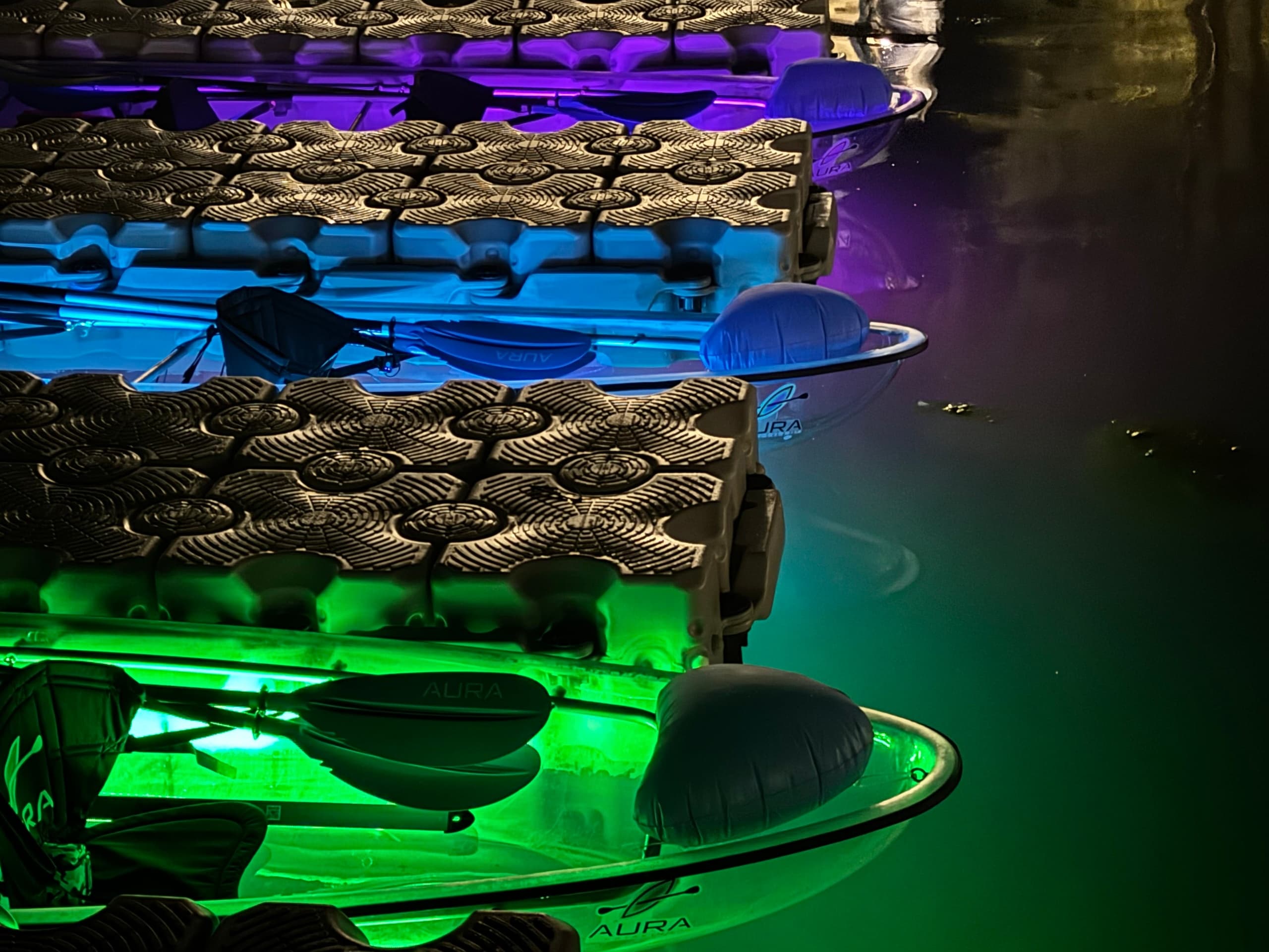 Stacked rental kayaks with colored LED lighting docked at night marina
