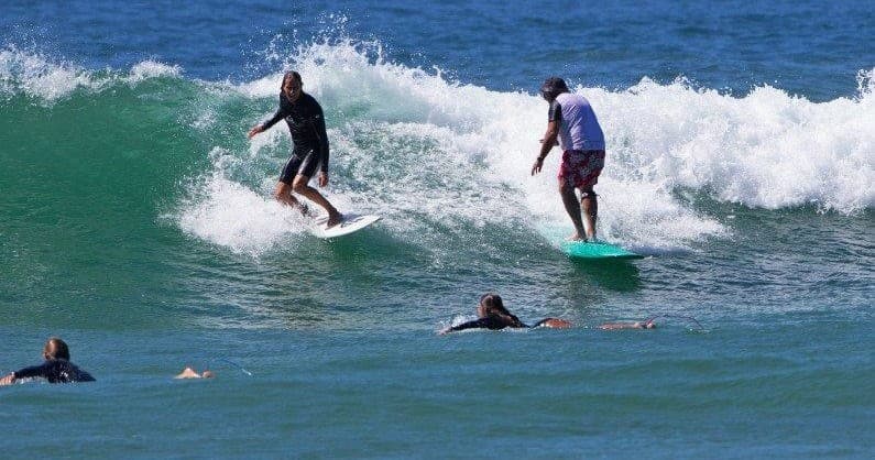 Multiple surfers riding small peel waves off Newcastle beach in group