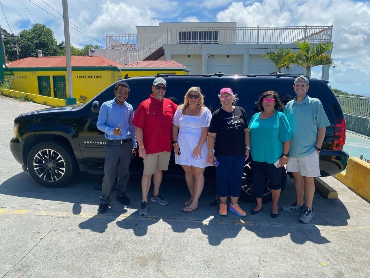 Tour group posing beside black SUV at tropical coastal parking