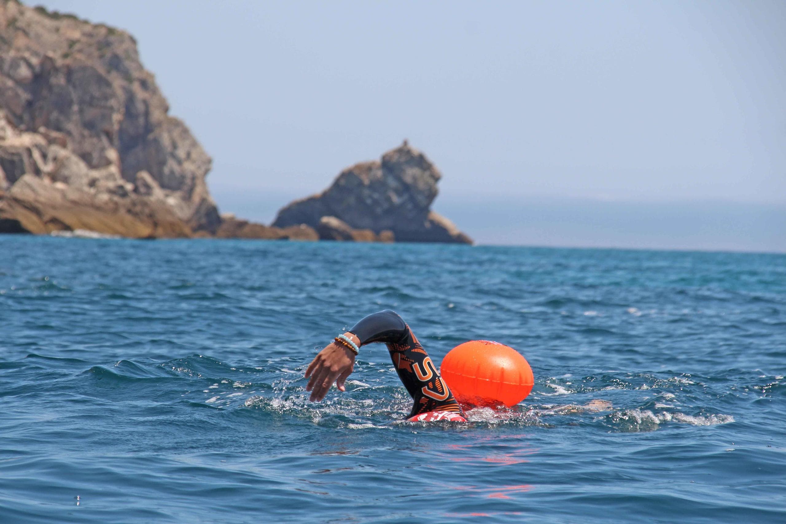 Solo swimmer with orange buoy in calm open-sea waters
