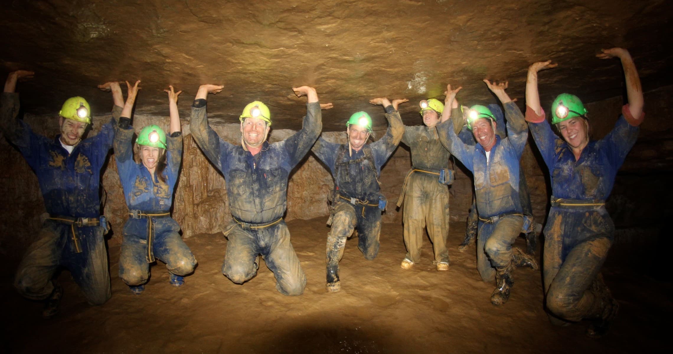 Group exploring underground cave passage wearing helmets and lamps