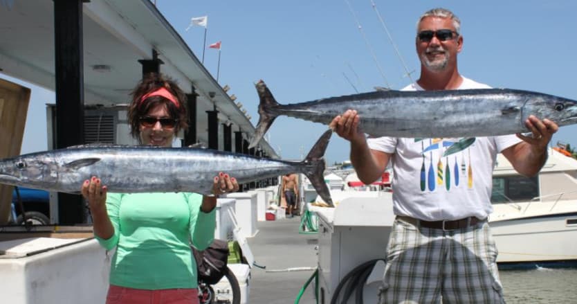 Couple displaying large wahoo catch at marina sportfishing dock