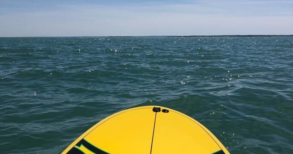 Bow of yellow paddleboard facing open ocean waves at horizon