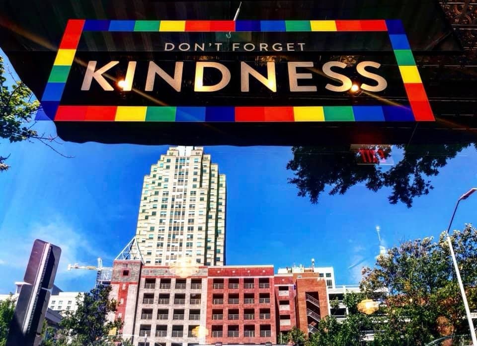 City skyline with colorful Kindness sign above downtown Raleigh street