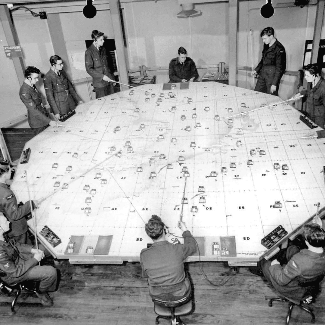 Military personnel plotting maps around large bunker table indoors