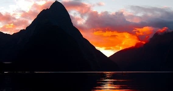 Towering fiord peak silhouetted at sunset over reflective water