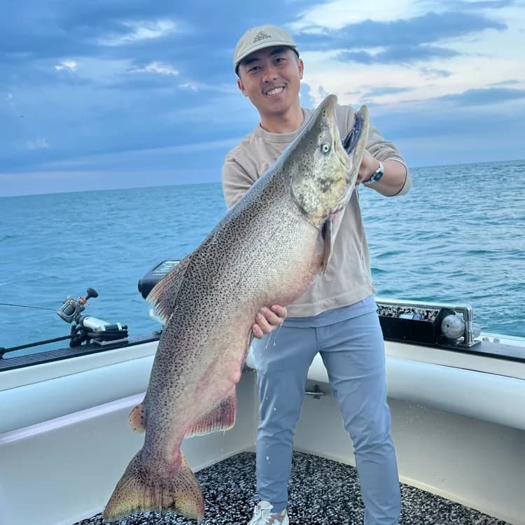 Angler holding massive lake trout aboard charter boat on open water