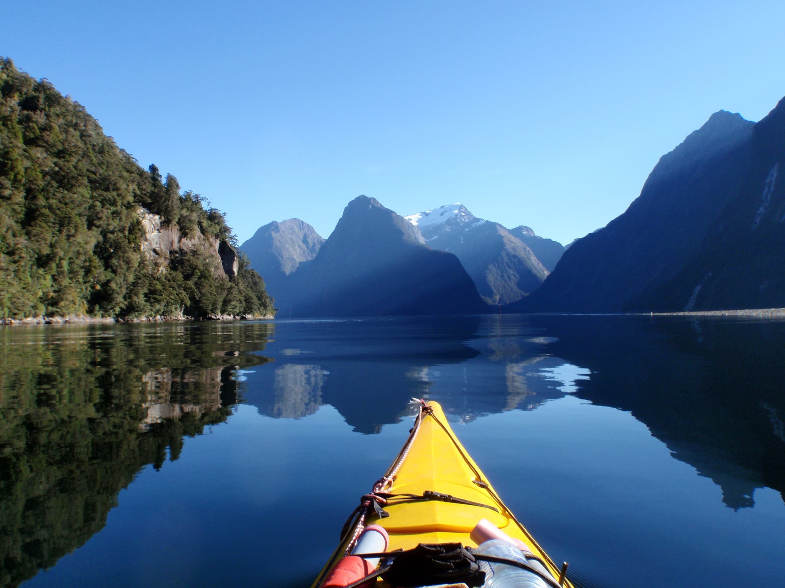 Single kayak paddling toward Milford Sound fjords on calm water