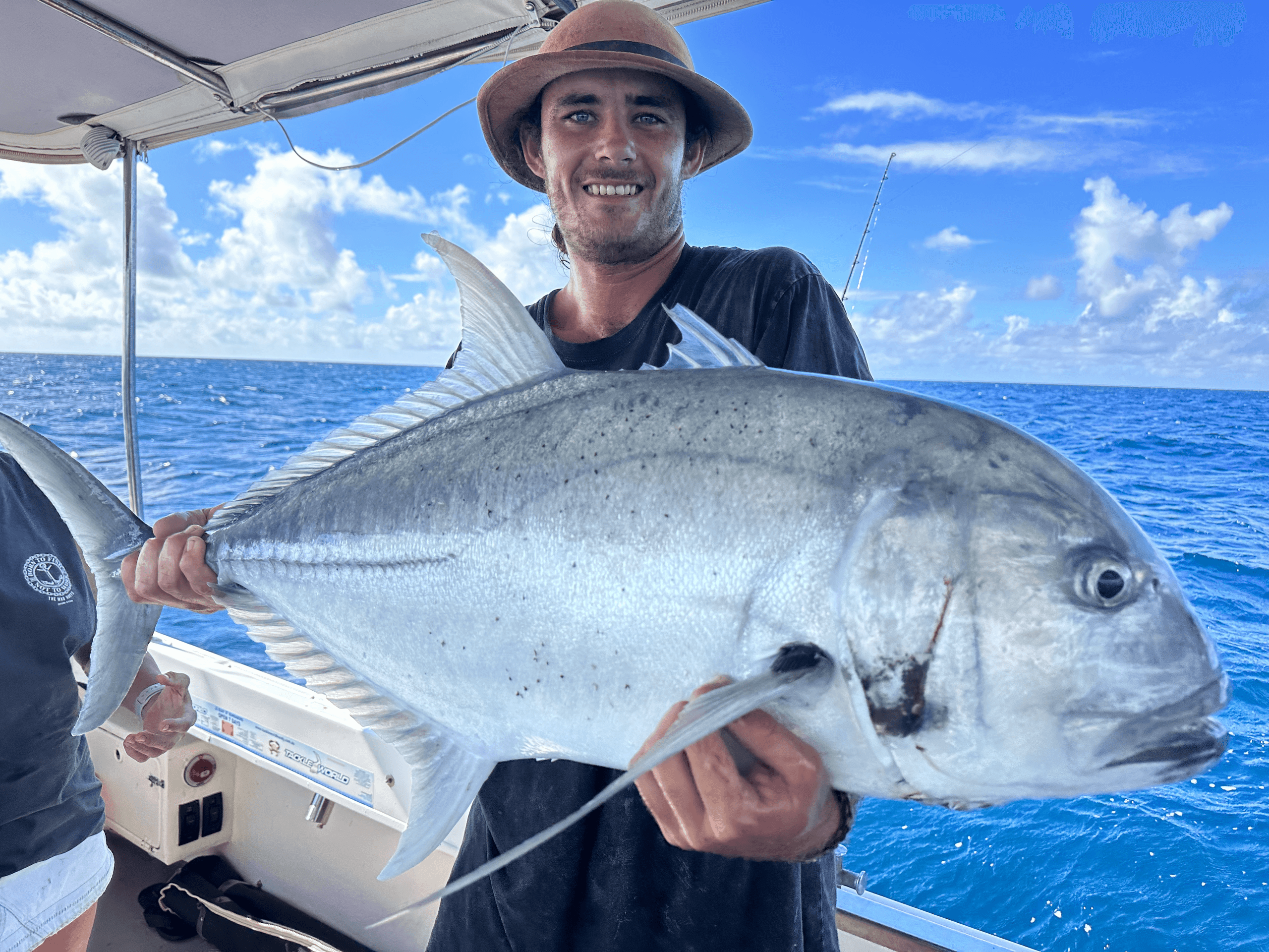 Angler holding giant trevally on sportfishing boat in open ocean