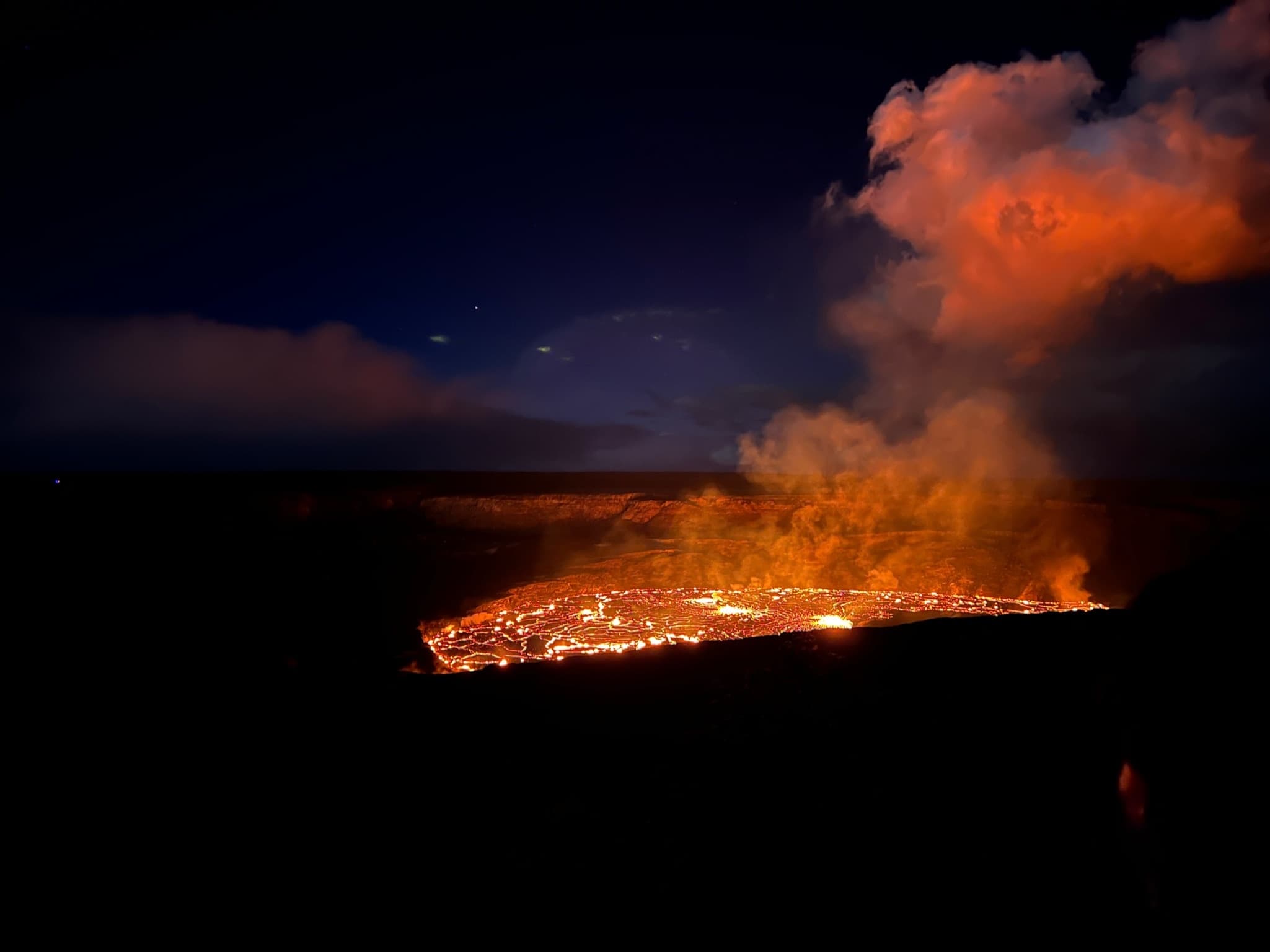Nighttime lava lake glowing in Kilauea caldera with orange plume