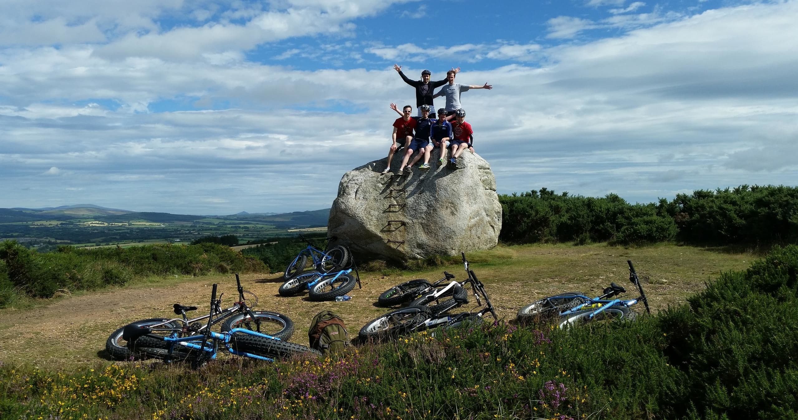 Group fatbikers celebrating on hilltop rock with bikes