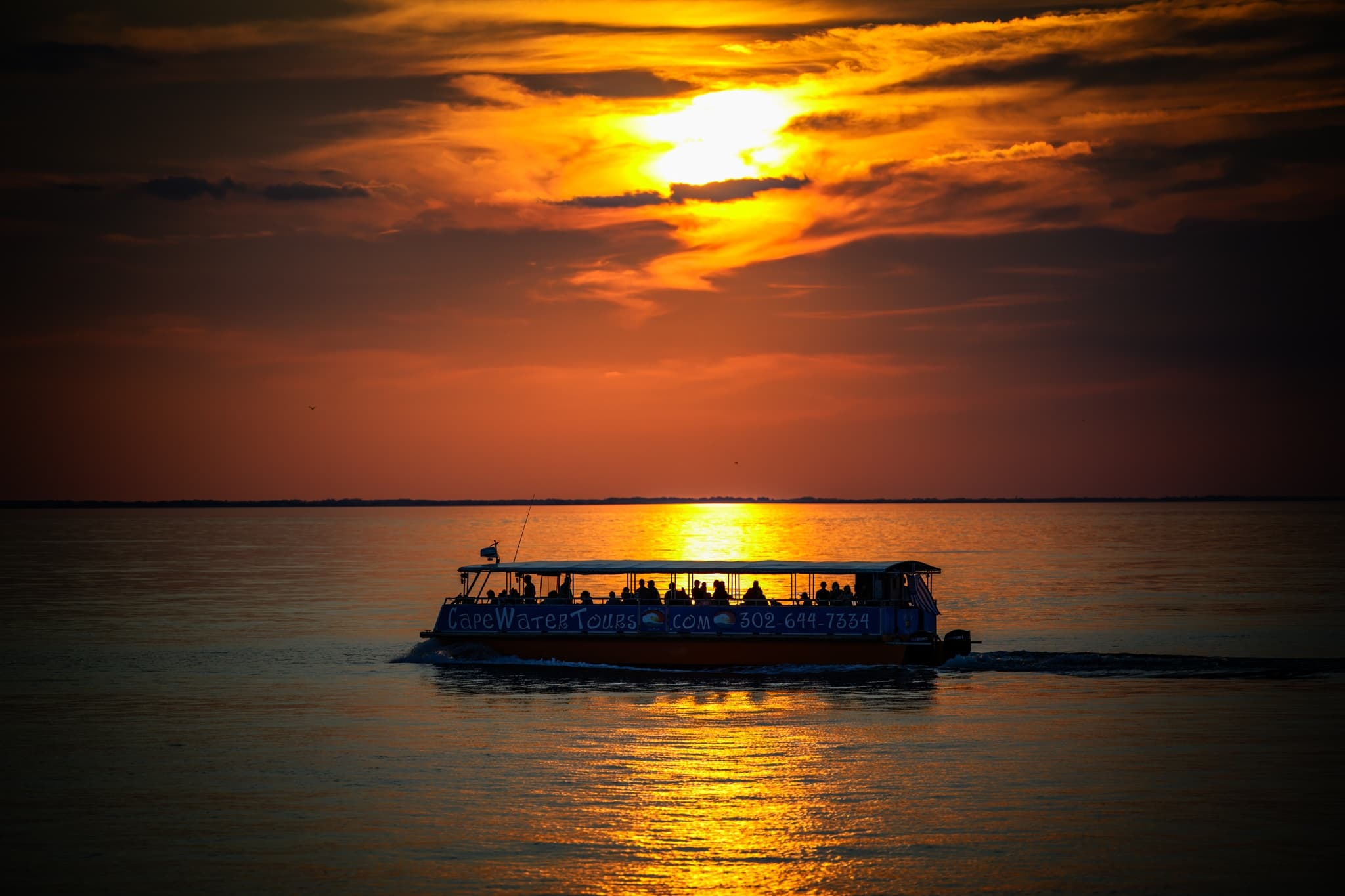 Sunset cruise boat silhouetted on calm ocean horizon