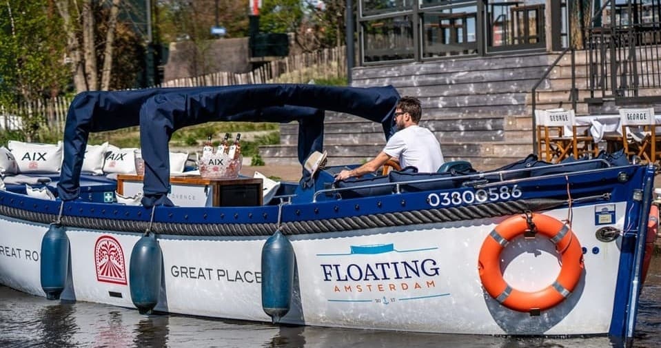 Floating Amsterdam branded boat docked along scenic canal