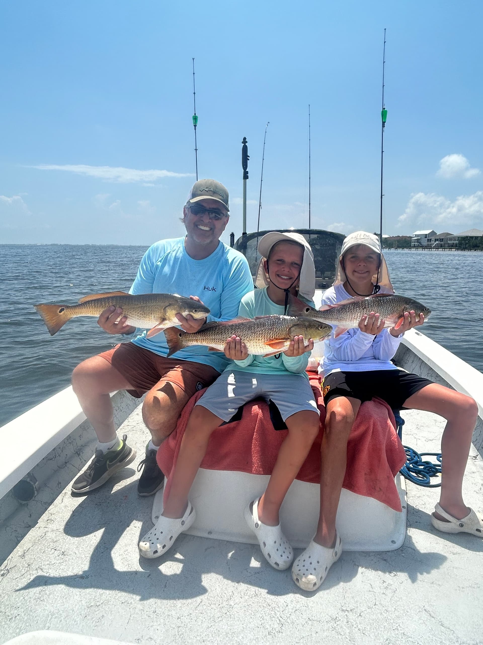 Family anglers seated on boat proudly holding multiple redfish