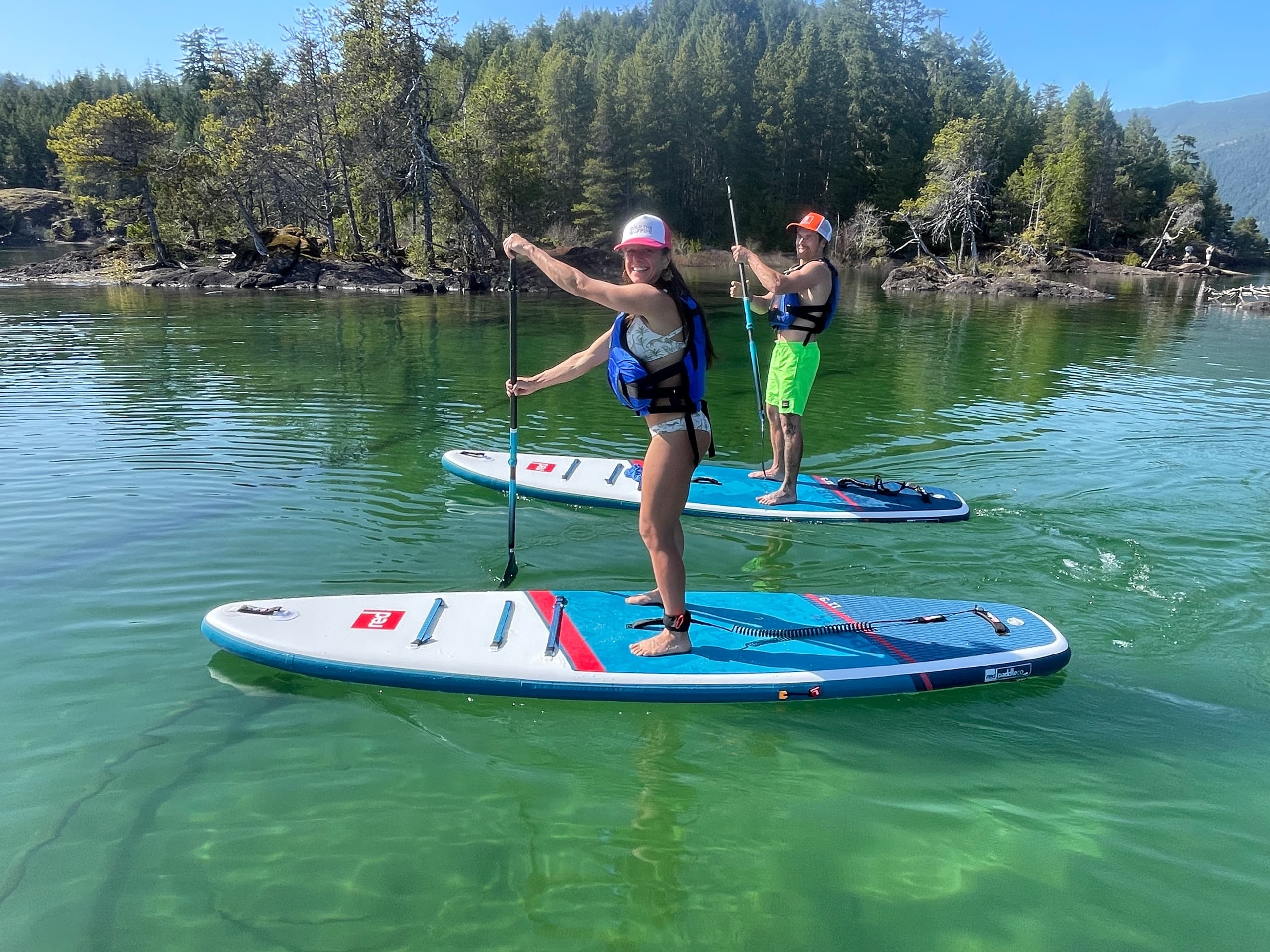 Two paddleboarders cruising on crystal-clear lake with forested shore