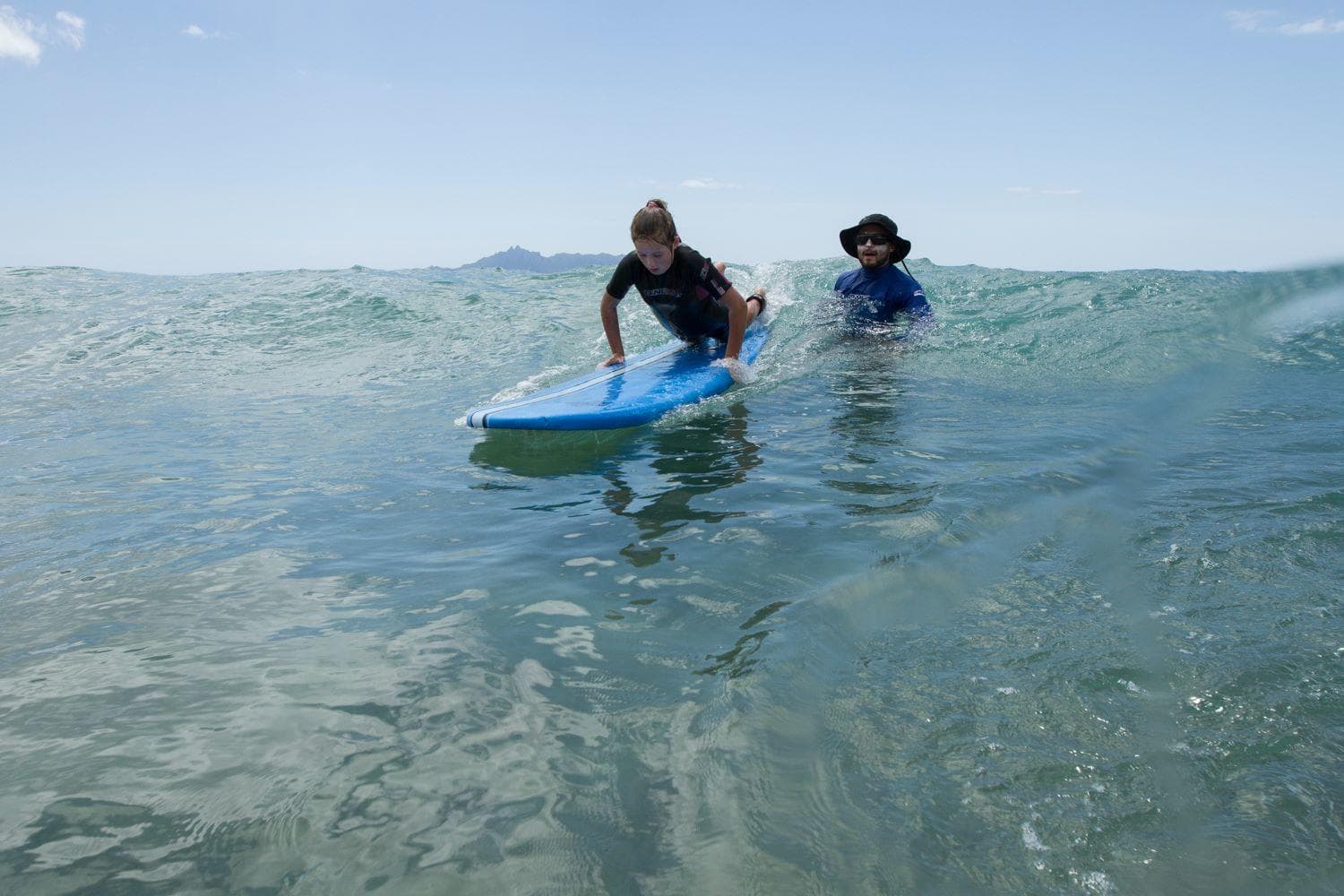 Instructor assisting student on surfboard in waist-deep ocean water