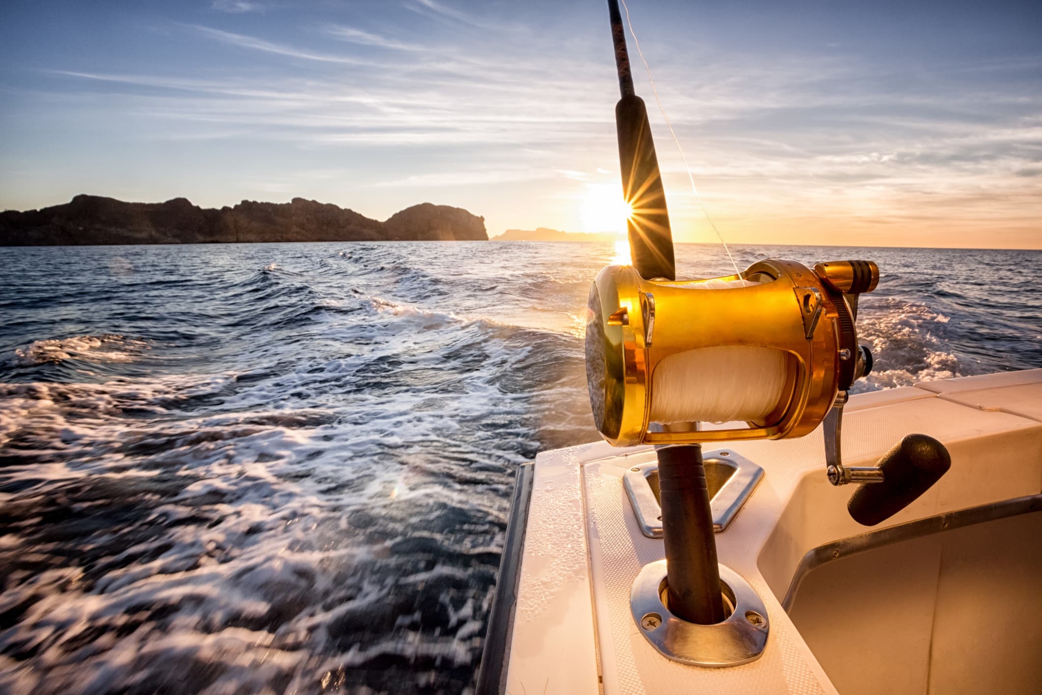 Deep-sea fishing reel on boat at sunrise with choppy seas