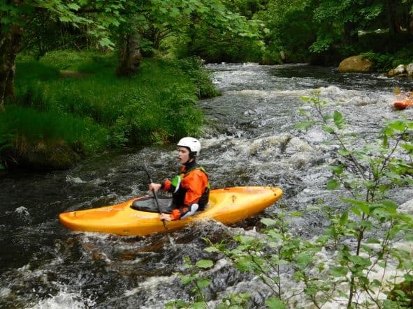 Kayaker paddling downstream on scenic forested river rapids