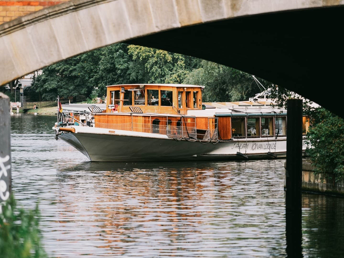 Small tour boat navigating calm city river under leafy banks