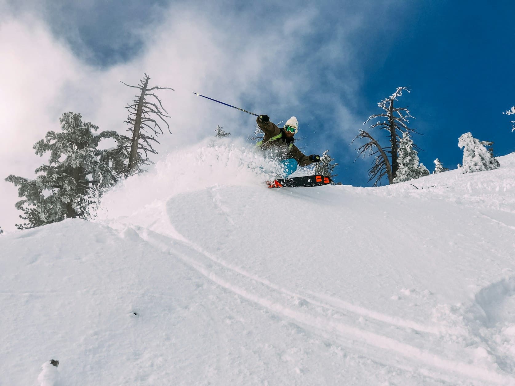 Snowboarder launching through deep powder on tree-lined slope