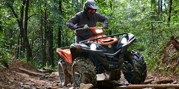 ATV rider navigating muddy forest trail through green woods