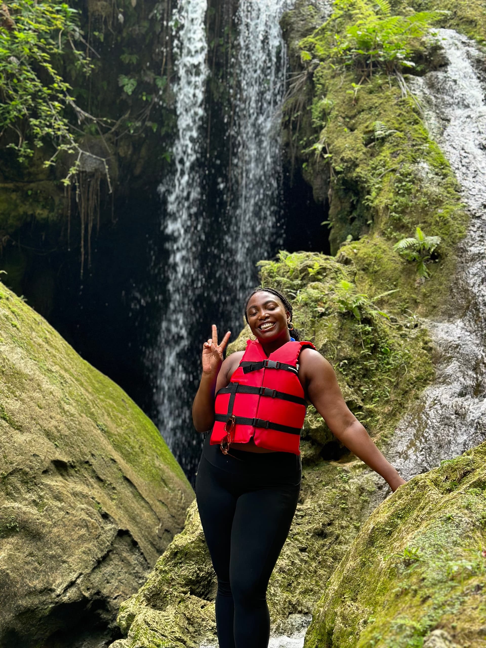 Hiker in red life vest smiling by mossy waterfall canyon