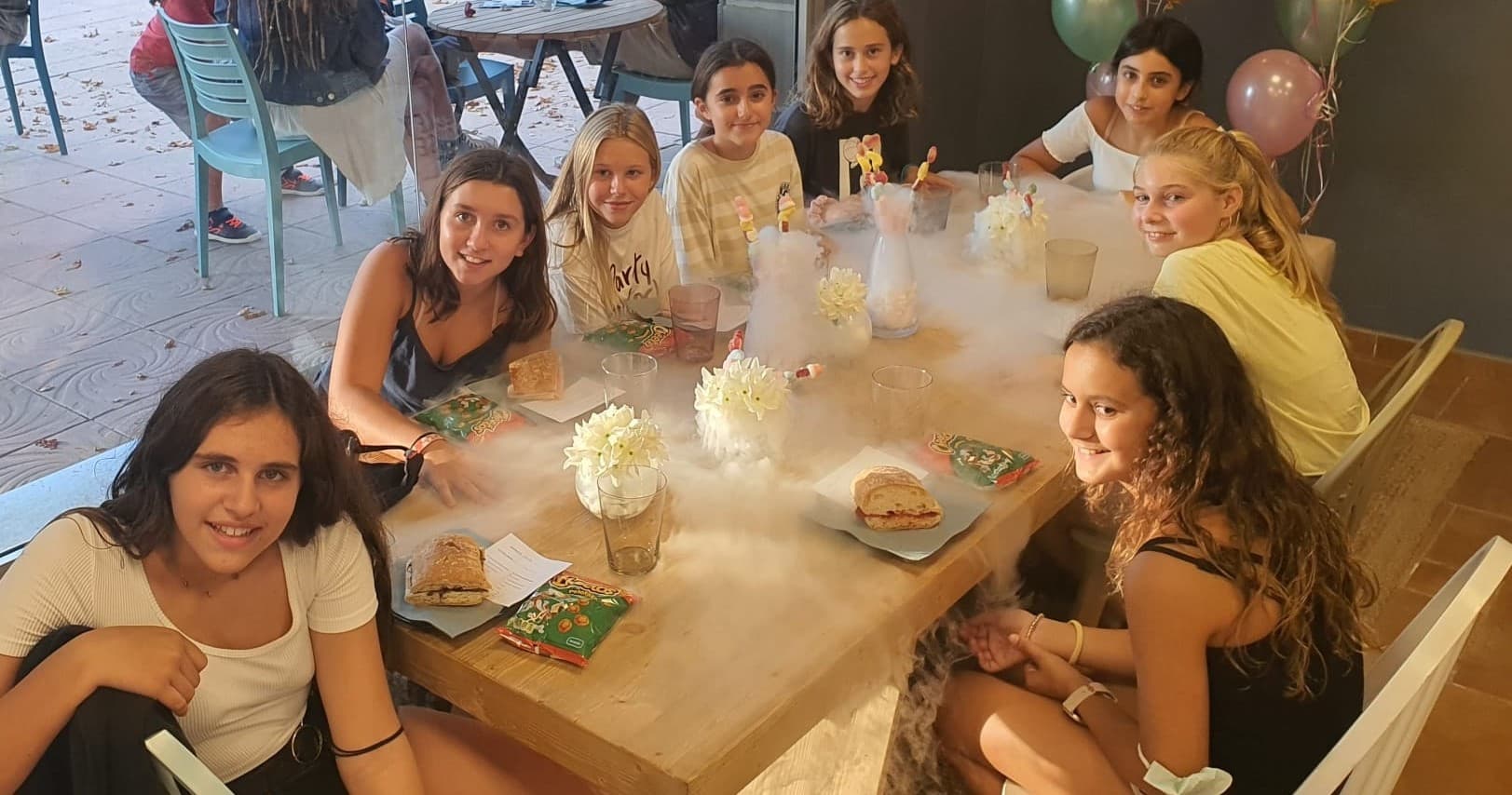 Friends enjoying outdoor patio birthday party with food and balloons