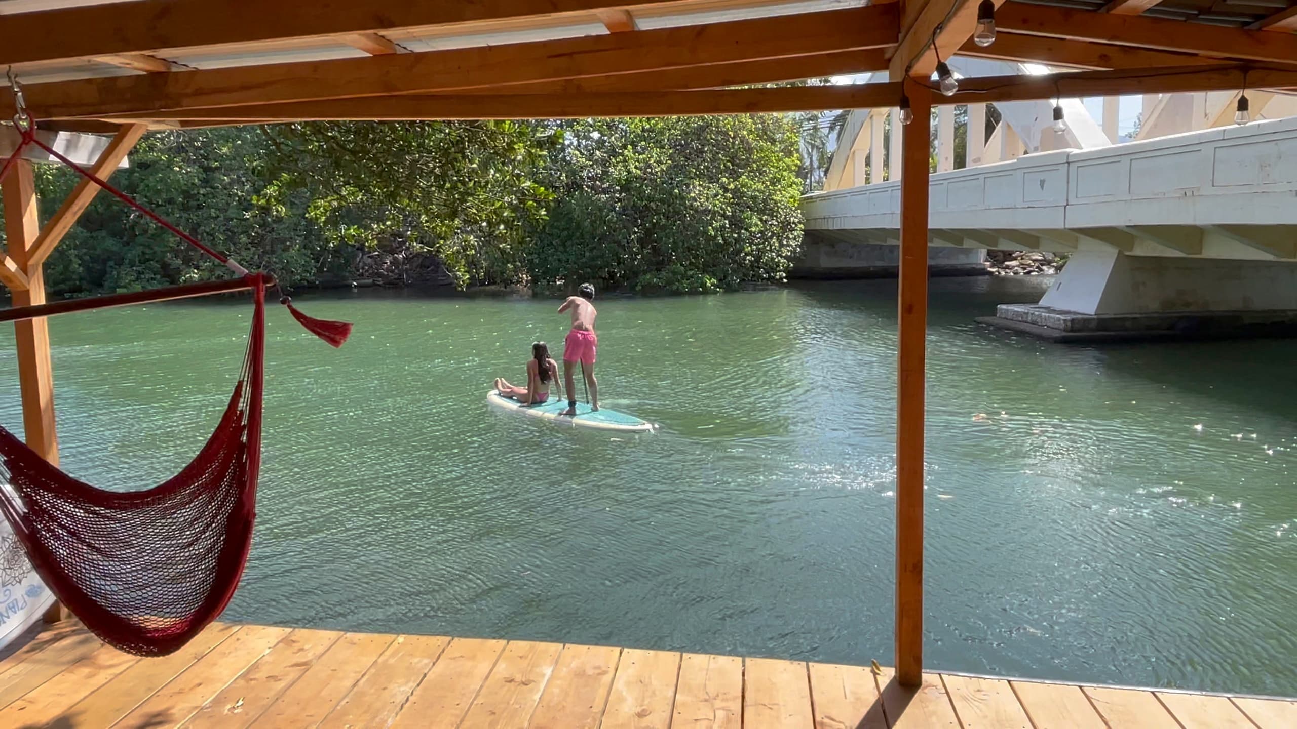 Stand-up paddleboarding near wooden dock and hammock by river
