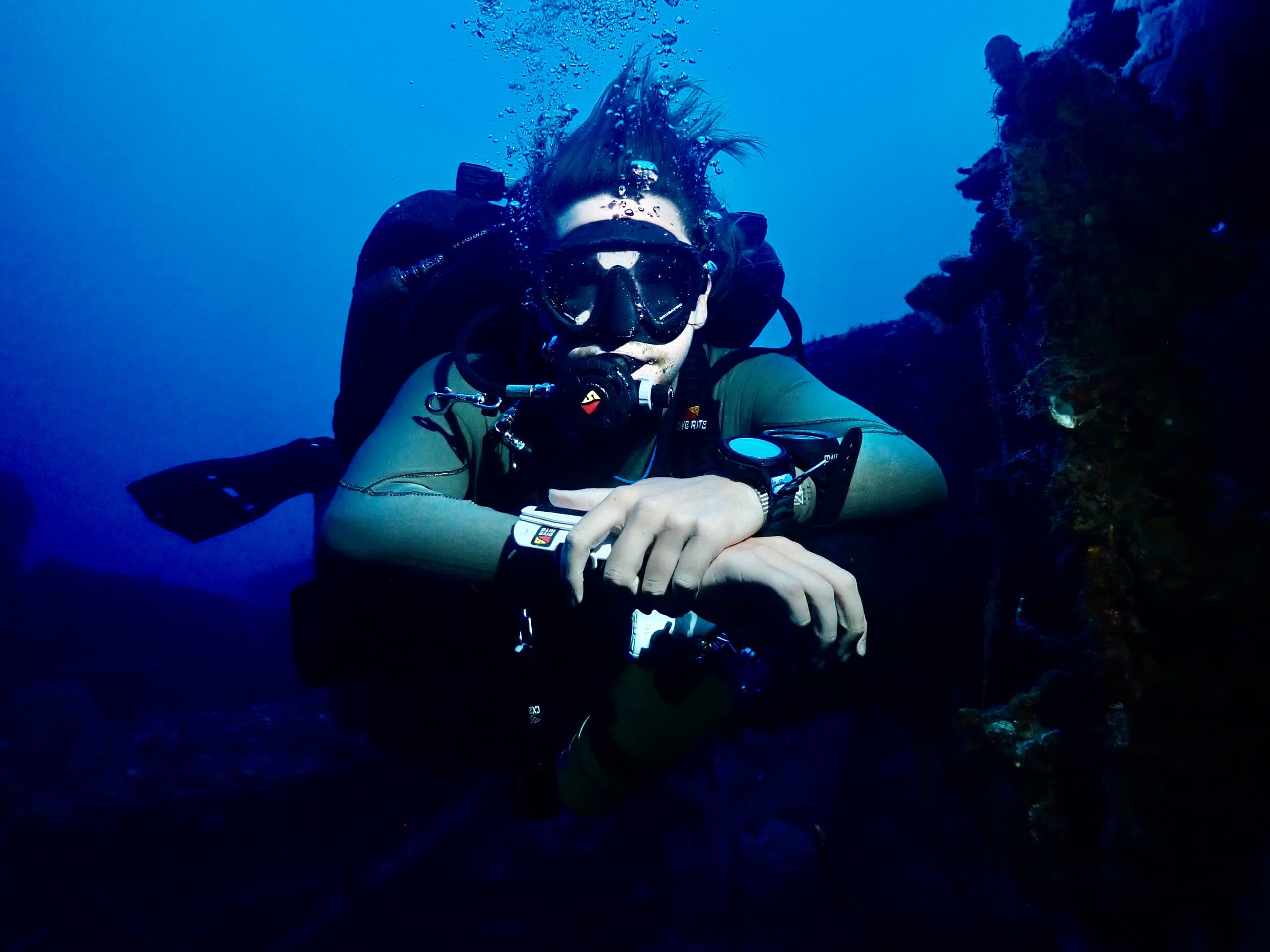 Close-up scuba diver underwater with regulator near reef wall