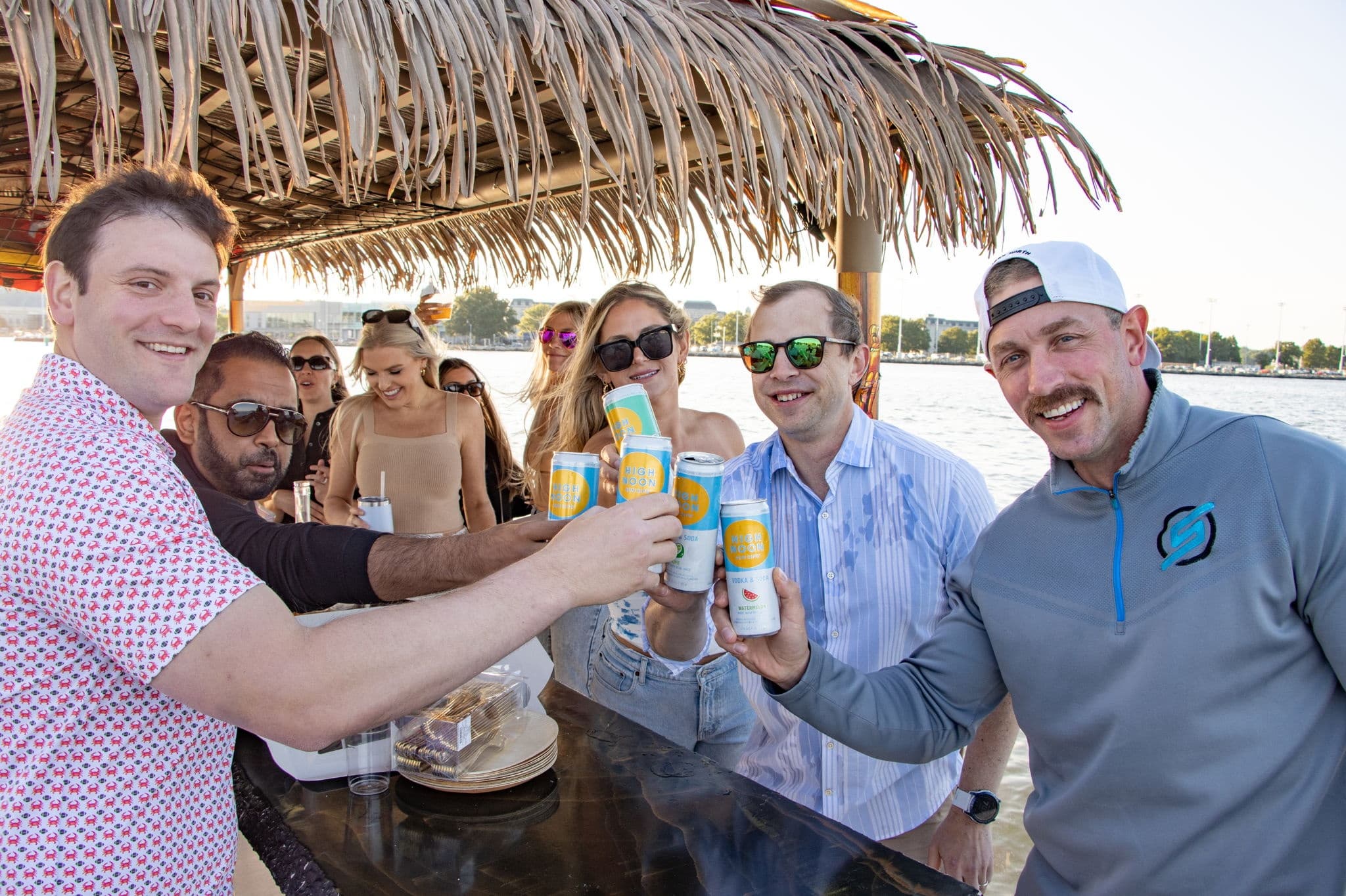 Friends toasting drinks on floating tiki bar cruise near marina