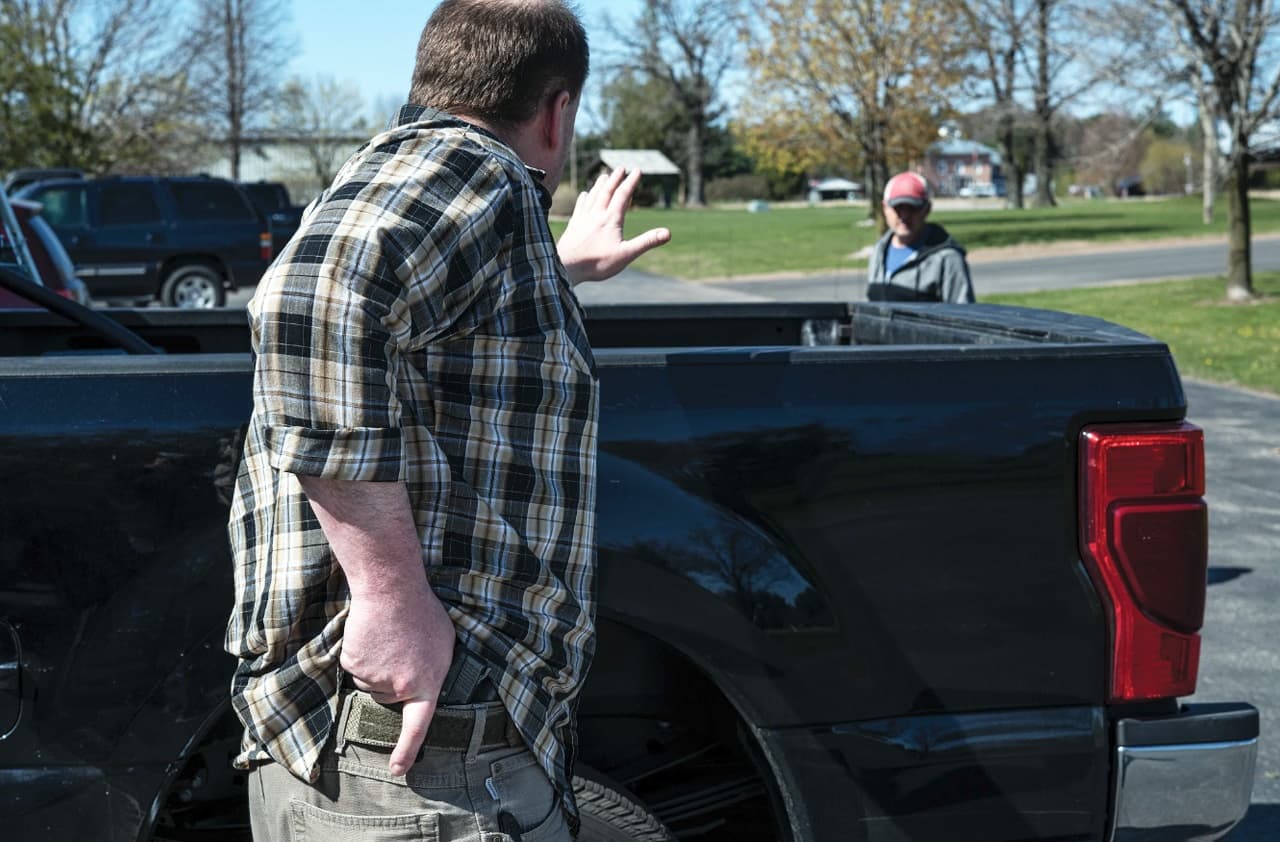 Man drawing handgun from pickup truck in outdoor park setting