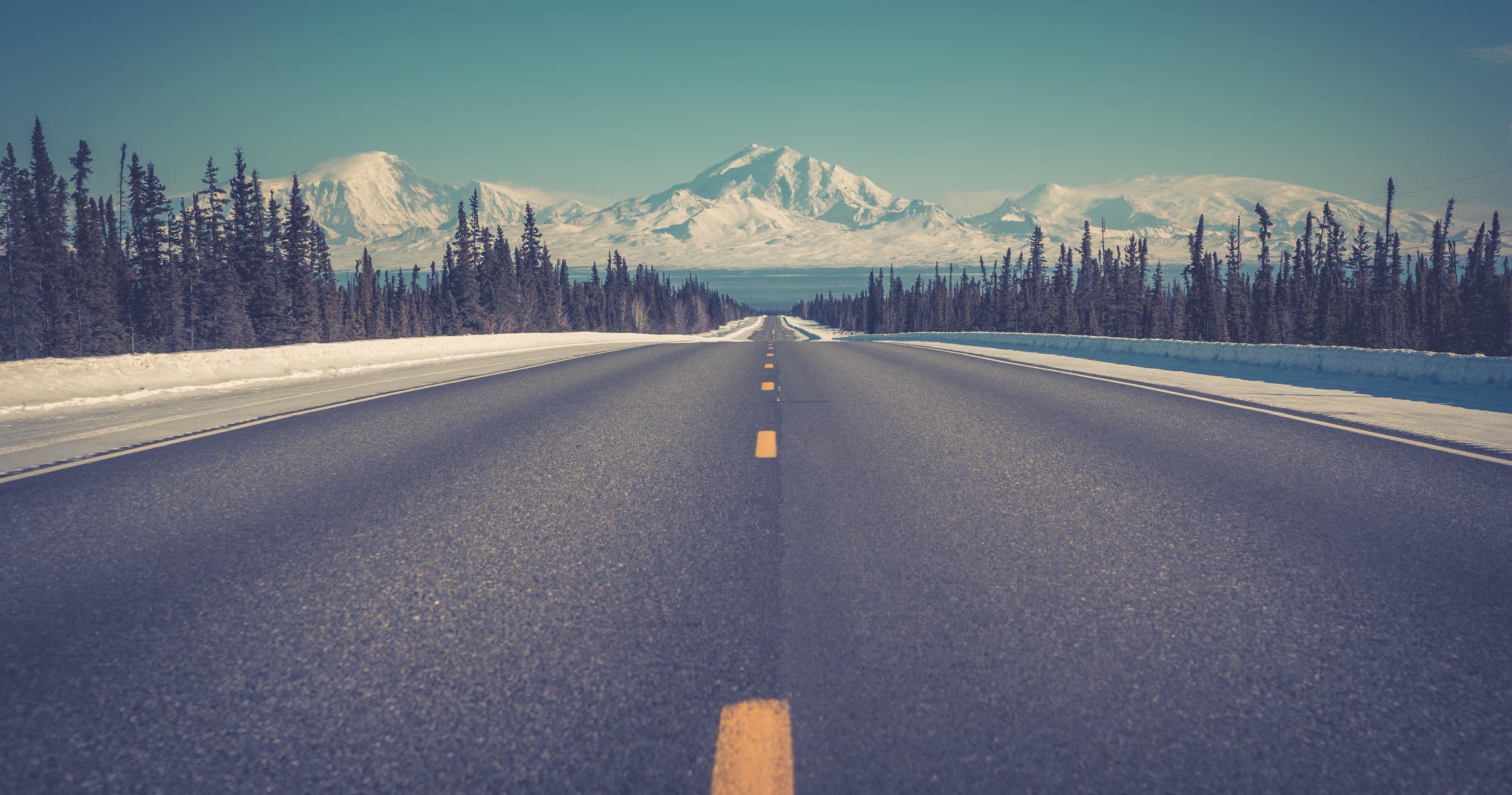 Open highway leading toward snow-capped Alaska mountain range