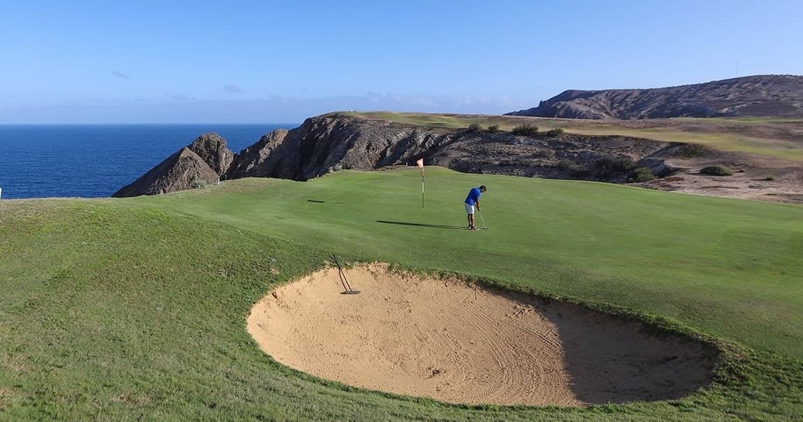 Golfer on coastal cliffside course with ocean and bunker