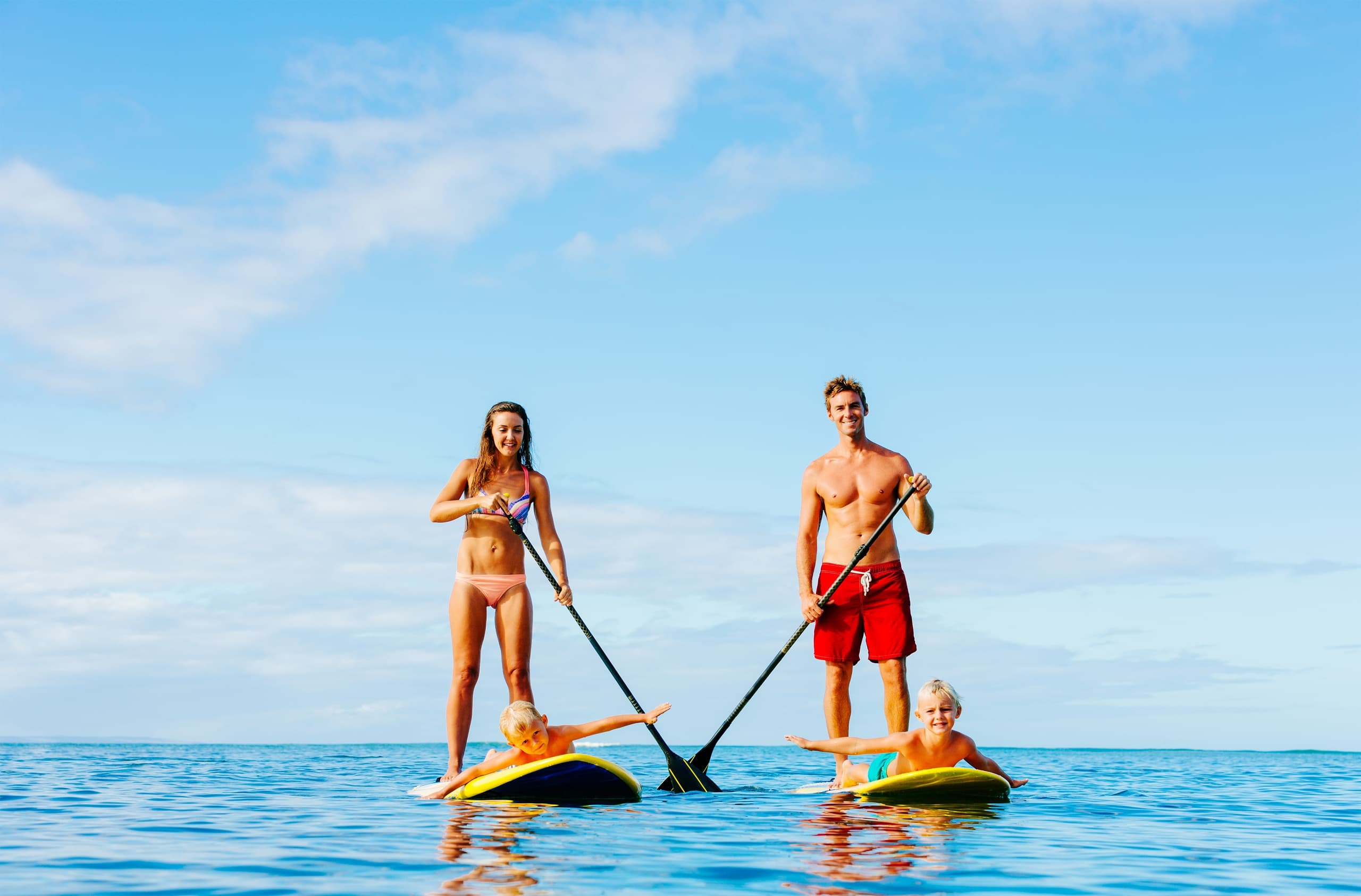 Family stand up paddleboarding on calm open sea under blue sky