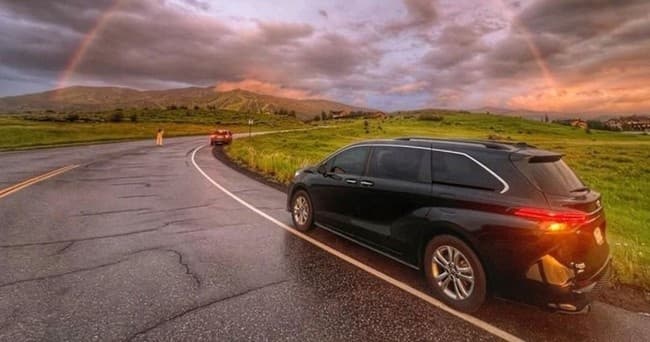 Minivan driving on scenic rural highway at sunset with rainbow