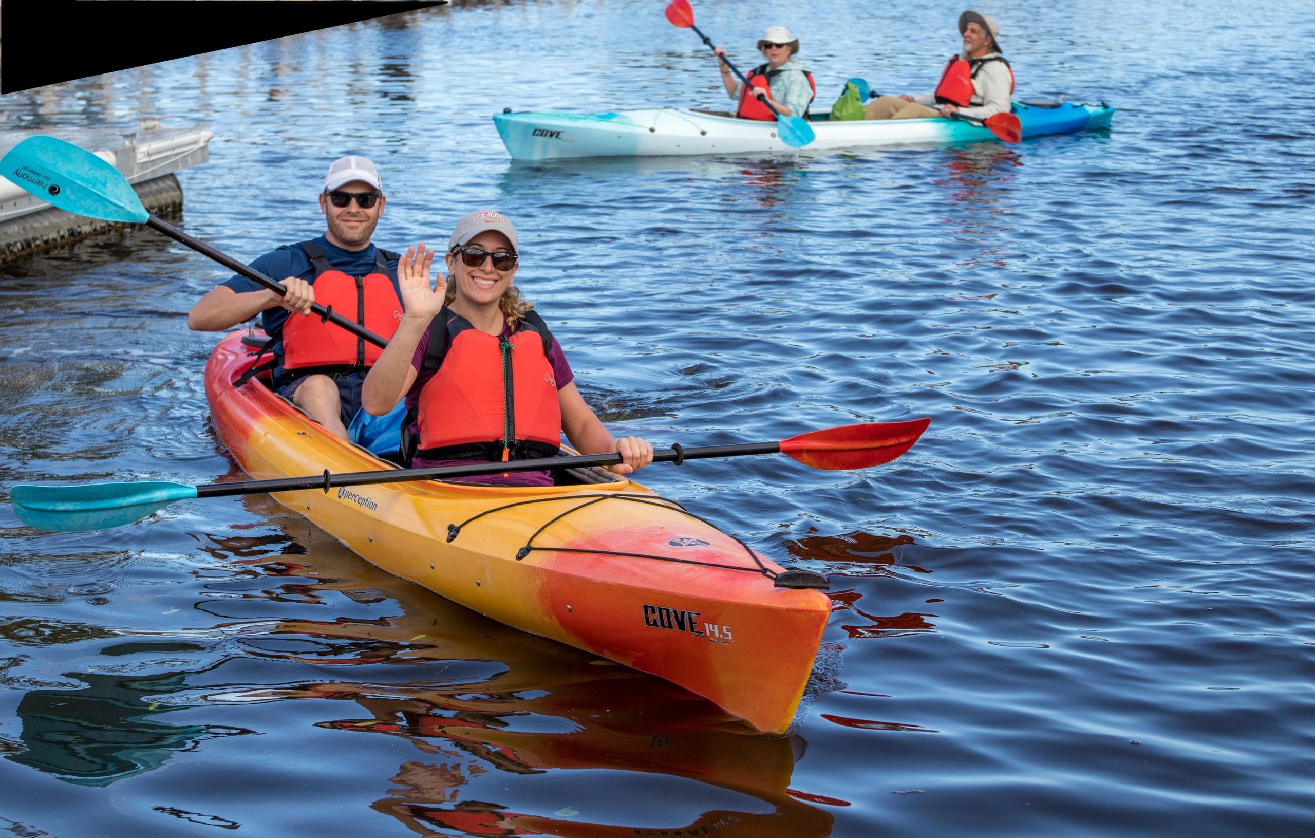 Tandem kayakers paddling colorful kayaks on scenic spring river