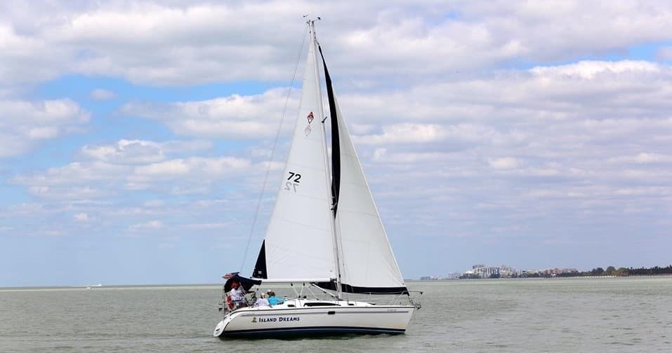 White-sailed yacht cruising on open water under cloudy sky near Naples