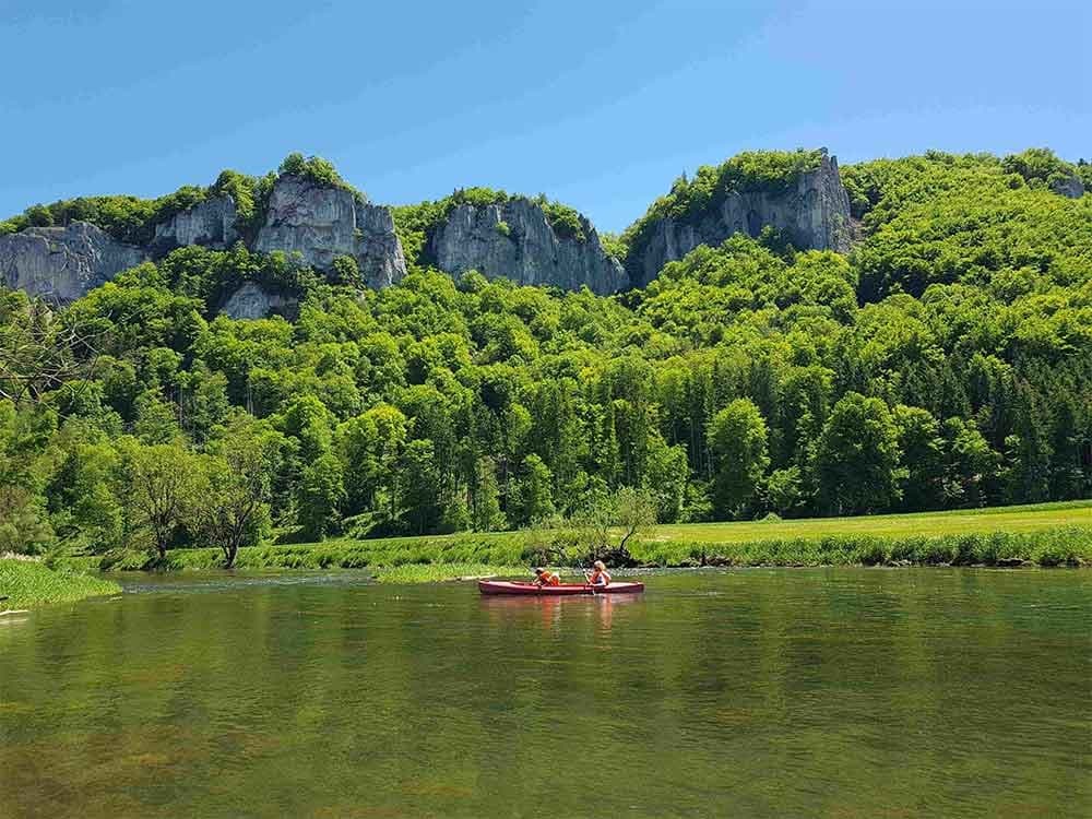 Kayakers paddling on calm river below limestone cliffs