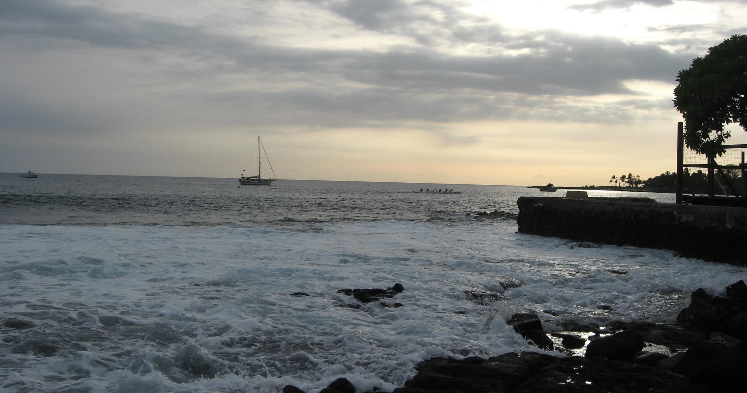Coastal shoreline with sailboat at sunset, waves crashing