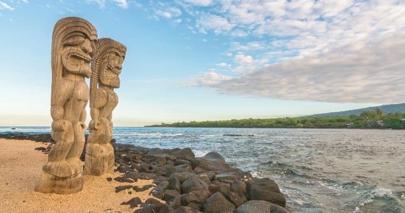 Tiki statues on sandy Hawaiian beach with ocean horizon
