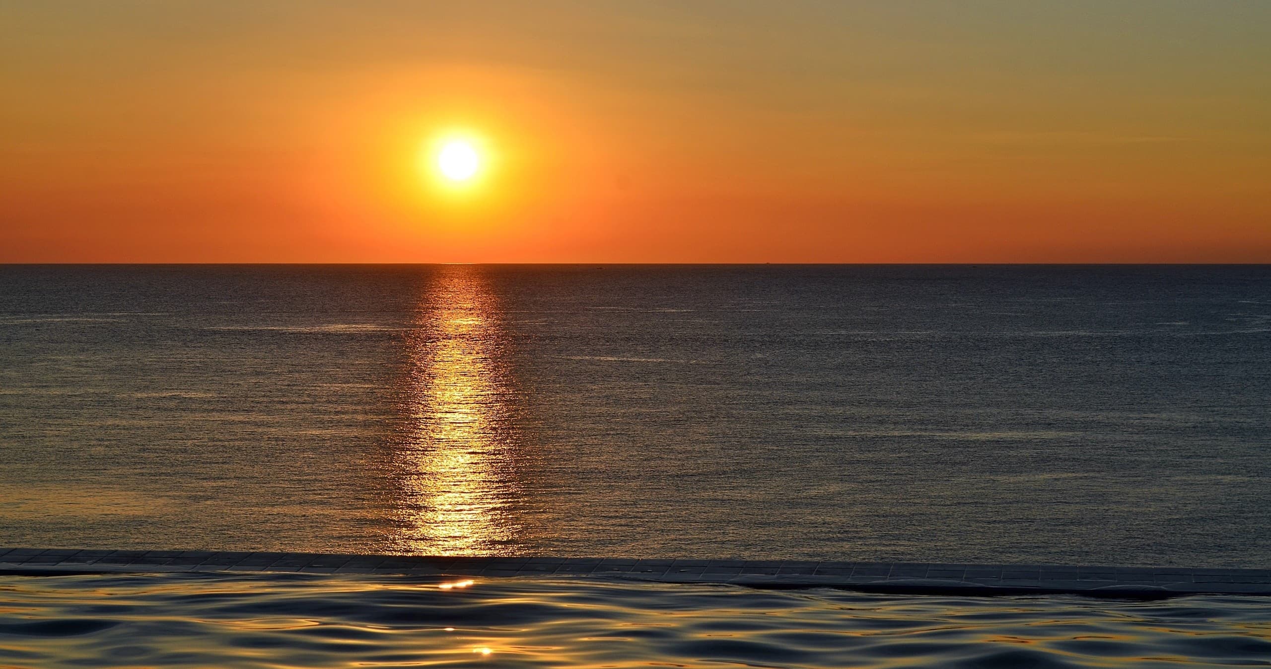 Sunset over open ocean with horizon reflection, beach viewing