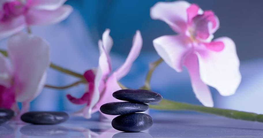 Zen spa stones with pink orchids on reflective surface